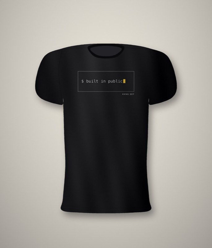 Black unisex tee with a terminal-style front print reading built in public, with a gold cursor block